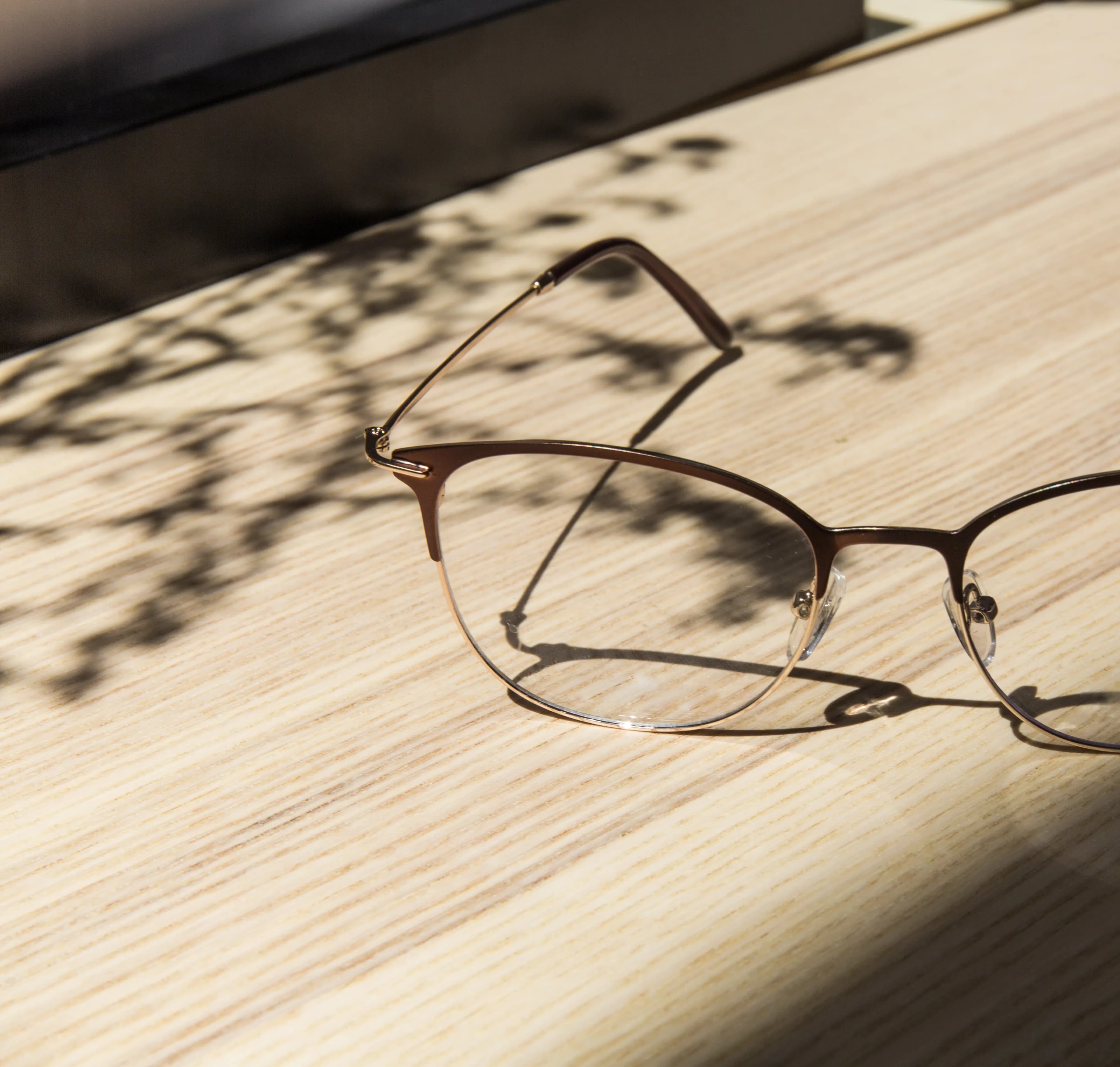 A pair of glasses resting on a wooden table in dappled sunlight